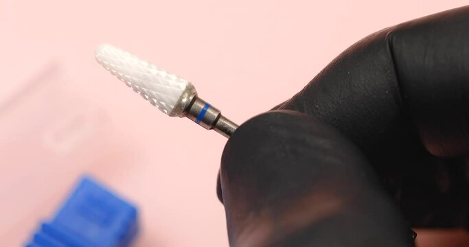 A specialist holds in his hands a cone-shaped ceramic cutter for hardware manicure with a blue notch for removing gel polish from nails