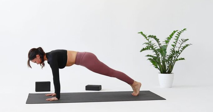 Athletic woman performs transitions from Chaturanga Dandasana exercise, plank pose to Adho Mukha Svanasana exercise, downward facing dog pose, practicing yoga on a mat in a bright room