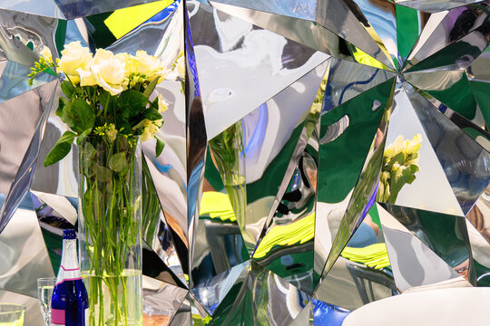 Table with a vase of flowers and a bottle of champagne against a bright mirror tringular background