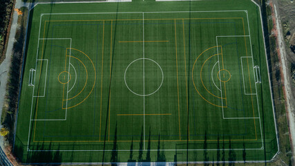 An aerial view of a green soccer field with lights and a path around it at sunrise © Matt