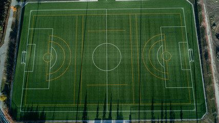 An aerial view of a green soccer field with lights and a path around it at sunrise