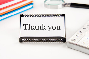 Text Thank You on a white business card on a table with office supplies