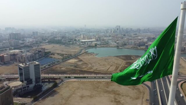 Aerial slow motion of the flag of Saudi Arabia fluttering in the wind on the tall poll