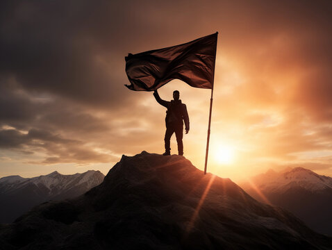 Backlit image of a Silhouette of a businessman holding a flag on the top of the mountain 