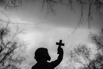 Silhouette of an angel statue, illuminated against a night sky, with a cross in his grasp
