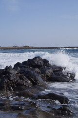 scogli vulcanici bagnati dalla marea dell'oceano, che crea un forte contrasto tra il bianco della schima e le pietre scure della costa