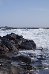 scogli vulcanici bagnati dalla marea dell'oceano, che crea un forte contrasto tra il bianco della schima e le pietre scure della costa