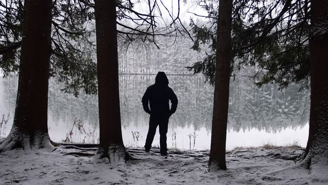 Man in silhouette standin by the shore of a stuning lake during winter fresh snow fall