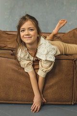 A cute and happy little girl is sitting on the sofa. Teenage girl. The girl is playing and enjoying...