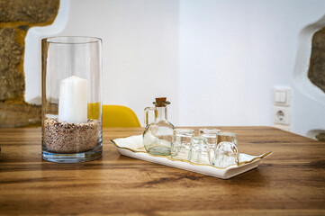 Close-up composition captures the cozy ambiance of a tabletop setting, featuring a flickering candle nestled within a glass vase. Adjacent, a stylish tray holds a carafe and small glasses