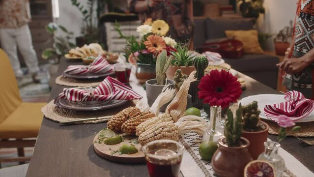 Medium shot of hands of two anonymous Mexican or Hispanic women putting plates with roasted corn, tacos, salsa and guacamole on table for feast, celebrating national holiday or family event - Powered by Adobe