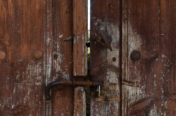 Front view closeup of antique wooden large double barn door with brown wood texture and metallic rusty vintage handle and bolts from a spain village. Architecture grunge vintage doors background. - obrazy, fototapety, plakaty