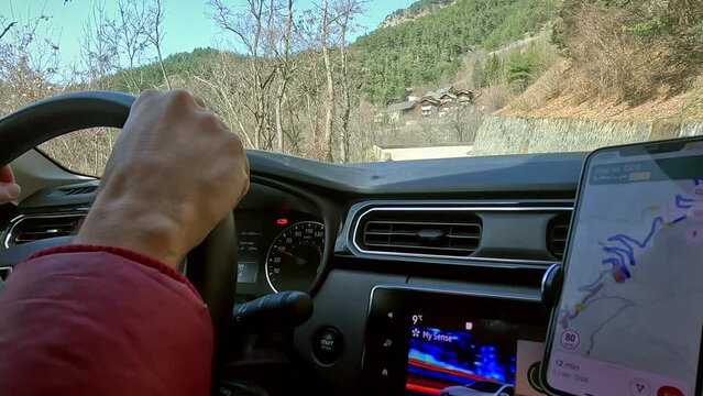 Hands on the steering wheel and online navigation. Driving the car along the windy road in the French Alps