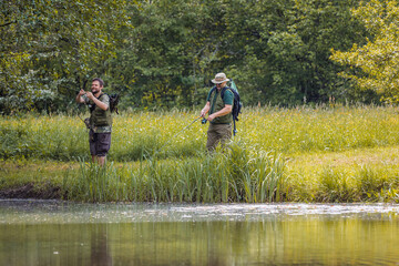 Senior and young fishermen on river shore having fun fishing and talking. Concepts of enjoyment and recreation in nature.