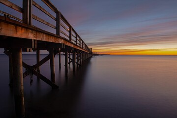 Wooden pier stretches out into a tranquil body of water at sunset.