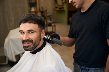 Barber using hair clipper for making stylish haircut for customer