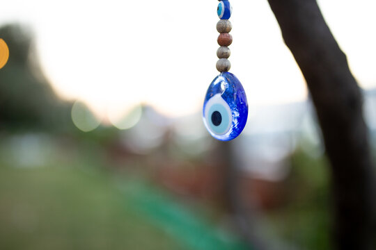 Close up of blue eye bead hanging on tree branch with bokeh background