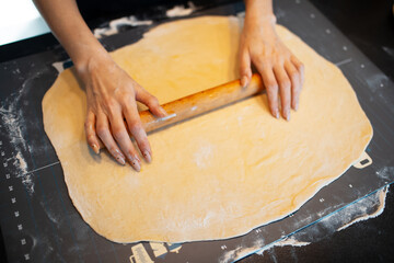 Top view of anonymous person hands rolling soft dough by rolling pin on table.