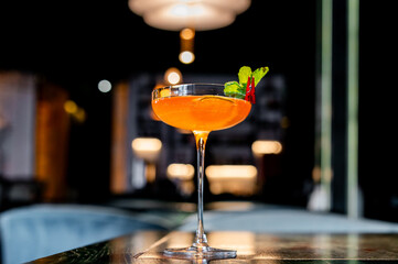 A vibrant orange cocktail, adorned with a fresh green leaf, rests elegantly on a dimly lit bar...