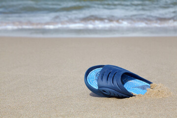 One blue rubber slate slipper on a deserted sandy beach. Forgotten and lost things