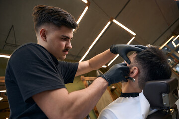 Barber master doing beard styling in barbershop