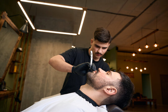 Barber master doing beard styling in barbershop