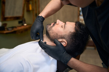 Bearded man getting shaved with straight edge razor by hairdresser