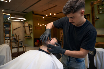 Bearded man getting shaved with straight edge razor by hairdresser