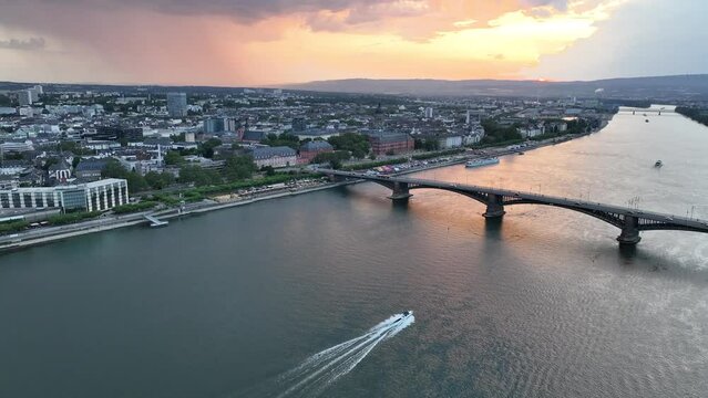 Drone shot of speed boat sailing on Rhine River going under Theodor Heuss Bridge at sunset, Germany