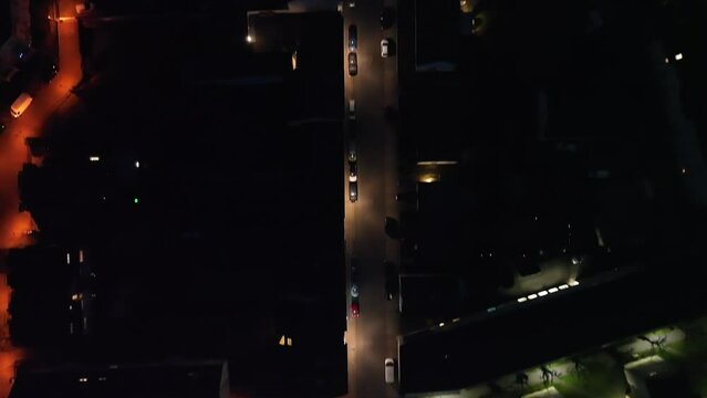 Drone footage of parked cars and cars driving on the city streets at night