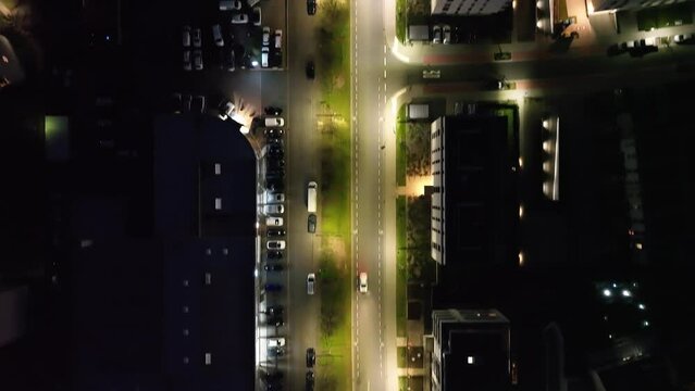 Drone footage of parked cars and cars driving on the city streets around a square at night