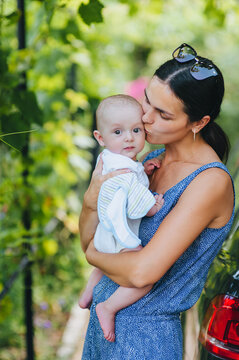 A beautiful young smiling brunette woman holds a small child, her son, in her arms outdoors in nature. Photo of a happy family, portrait of people, lifestyle.