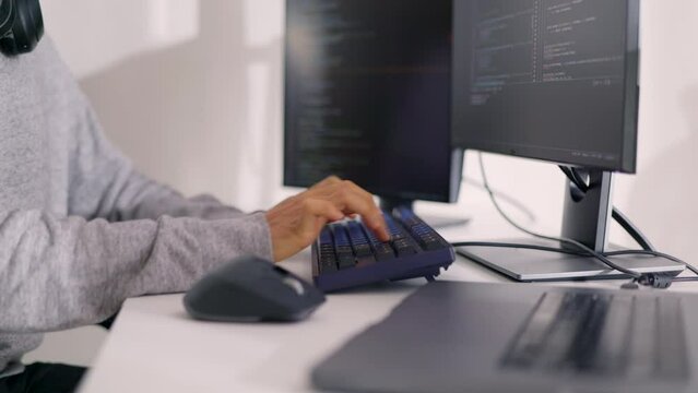 Close-up of a programmer's hands typing on a keyboard with code on a monitor, depicting focused work on software development.