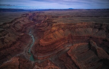 a desert area with sparse dirt and brown rock, a river running through the center