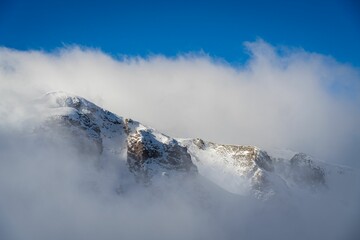 Majestic mountain peak surrounded by a blanket of white clouds against a deep blue sky, Montenegro