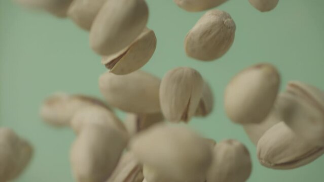 Flying in air fresh raw whole and cracked pistachios on green background. Pistachio nuts are falling in slow motion. Concept organic diet. Ungraded ProRes footage for grading