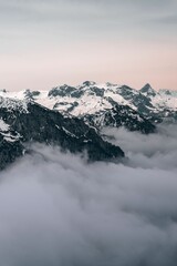 Fototapeta na wymiar Scenic view of snow-covered mountains surrounded by a blanket of fog and clouds in a cloudy sky