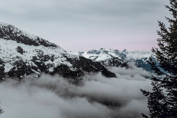 Fototapeta na wymiar Snow-covered mountain peak with white wispy clouds hovering around its peak in Berchtesgaden
