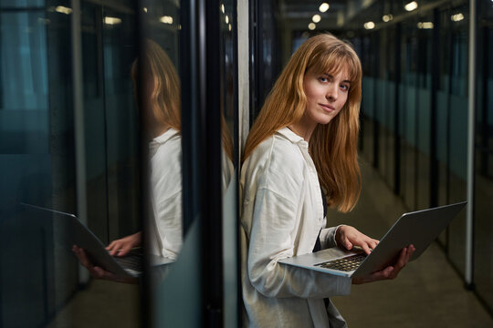Woman designer standing with laptop in office corridor