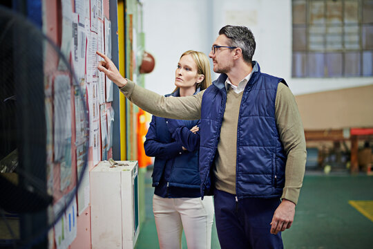 People, business and planning schedule with board in warehouse with calendar for order details. Man, woman and together for checking for supplier information or notes, inventory updates and targets.