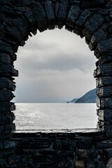 Stone archway leading to a stunning vista of the sea and the mountains beyond in Italy.