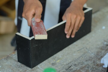 Hands of a carpenter manually sanding wooden with sandpaper in a woodworking or carpentry workshop