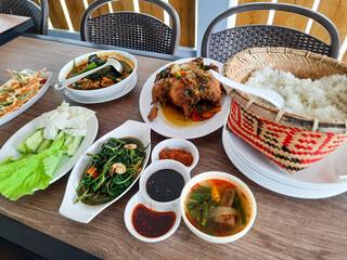 background of a diverse food menu from spiced fried chicken, stir-fried water spinach, fish curry, vegetable bakwan and fresh vegetables at the Kampong Laok restaurant