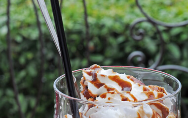 Whipped cream and chocolate sauce in an ice cream glass with silver spoon and black straw. Selective focus