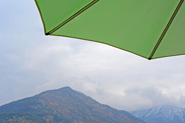 Green beach umbrella with mountains at Lake Como in the back on a clouded spring day. Selective focus