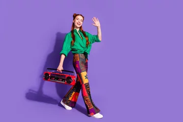 Poster Full length photo of pleasant pretty girl wear print vintage pants waving palm hold retro boombox isolated on violet color background © deagreez