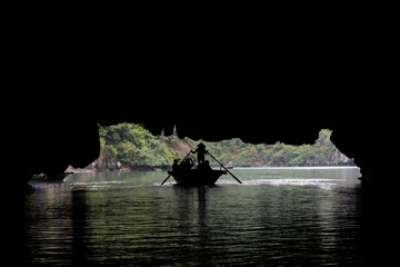 Silhouette of a small row boat passing through a cave on a river in Tam Coc, Vietnam.