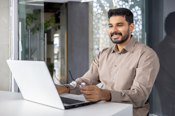 Happy young businessman working on laptop at desk in contemporary office setting, showing job satisfaction and professionalism.