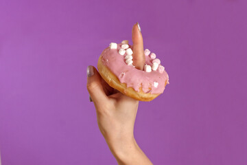 Pink donuts placed on one hand finger of a woman with purple painted nails on magenta background