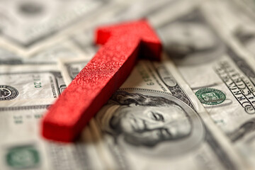 Red arrow pointing up on a background of hundred dollar bills
